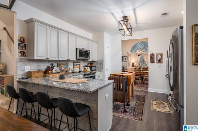 kitchen featuring visible vents, dark wood-type flooring, light stone counters, a peninsula, and stainless steel appliances