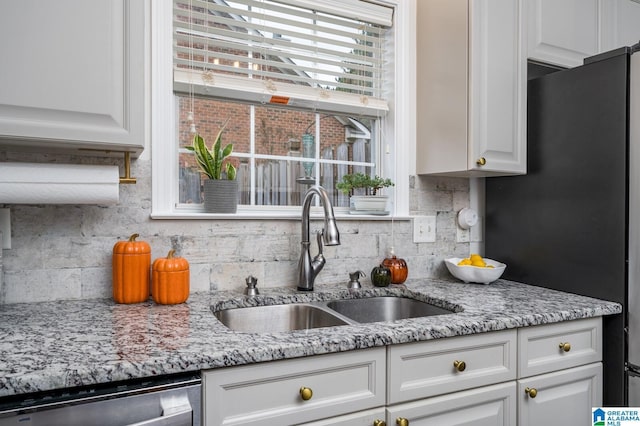 kitchen with backsplash, light stone countertops, appliances with stainless steel finishes, white cabinetry, and a sink