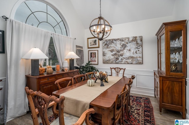 dining area with a wainscoted wall, a notable chandelier, wood finished floors, a decorative wall, and vaulted ceiling