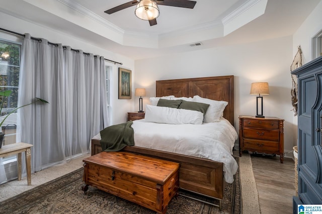 bedroom featuring a raised ceiling, a ceiling fan, wood finished floors, and crown molding