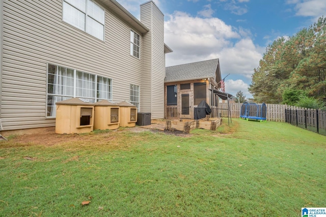 rear view of property with a fenced backyard, a yard, cooling unit, and a trampoline