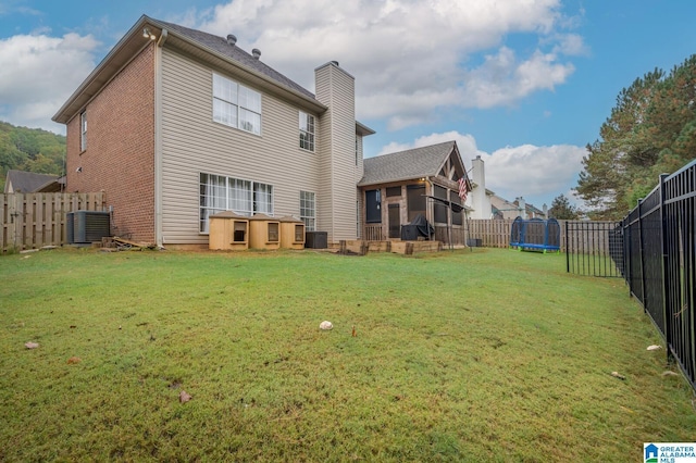 rear view of house featuring a trampoline, a lawn, and a fenced backyard