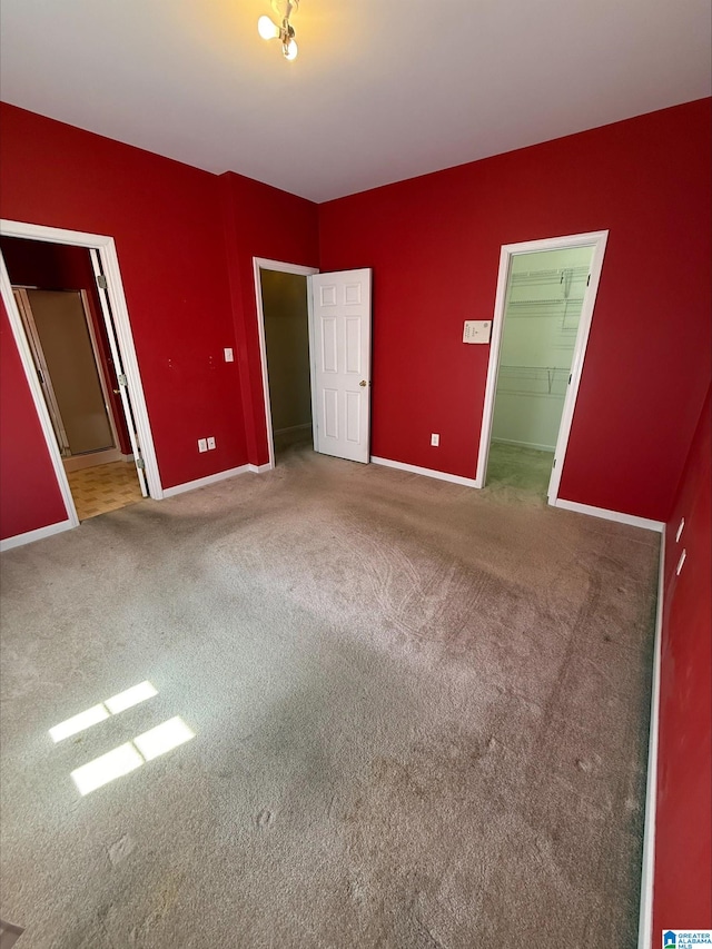 unfurnished bedroom featuring a walk in closet, baseboards, and carpet floors