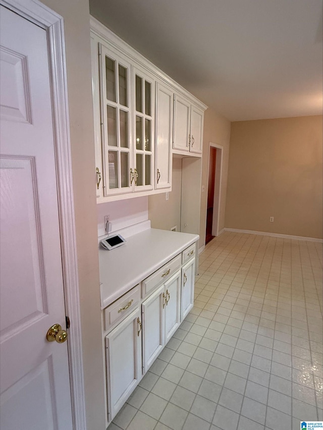 kitchen featuring light tile patterned floors, baseboards, light countertops, white cabinets, and glass insert cabinets