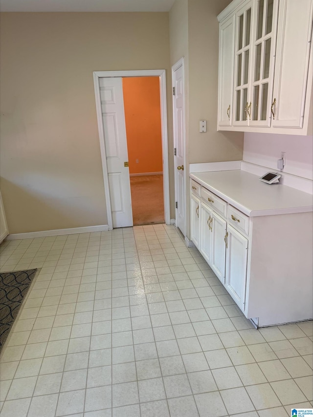 kitchen featuring white cabinets, light countertops, light tile patterned floors, glass insert cabinets, and baseboards