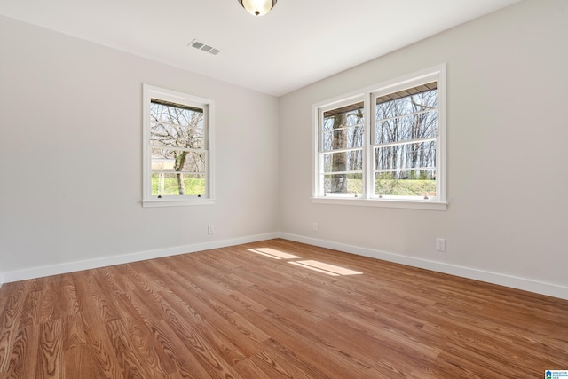 empty room with wood finished floors, visible vents, and baseboards