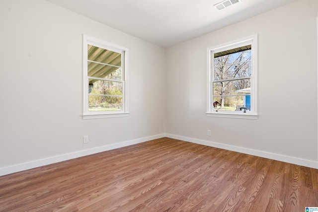 spare room featuring wood finished floors, visible vents, and baseboards