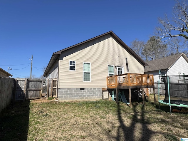 back of house with a fenced backyard, a yard, a wooden deck, and a trampoline