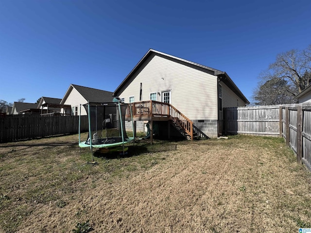 rear view of property with a yard, a deck, a trampoline, and a fenced backyard