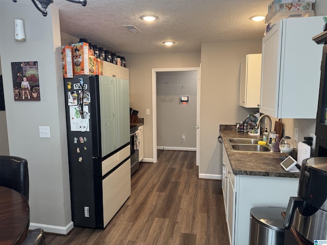 kitchen with white cabinetry, dark countertops, freestanding refrigerator, and a sink