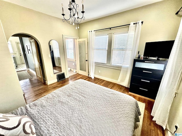 bedroom featuring baseboards, arched walkways, wood finished floors, and a chandelier