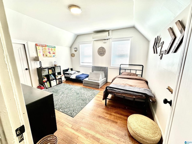 bedroom featuring a wall unit AC, wood finished floors, baseboards, and vaulted ceiling