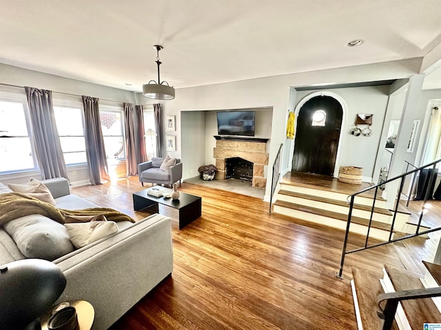 living room featuring wood finished floors, arched walkways, a stone fireplace, baseboards, and stairs