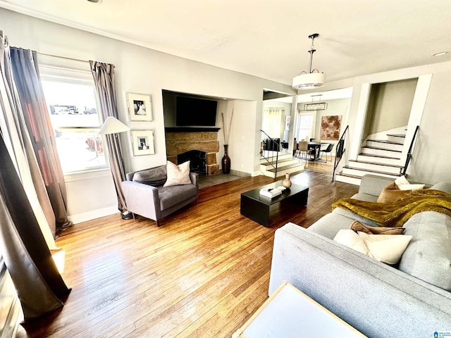 living area with baseboards, a stone fireplace, light wood-style flooring, and stairs