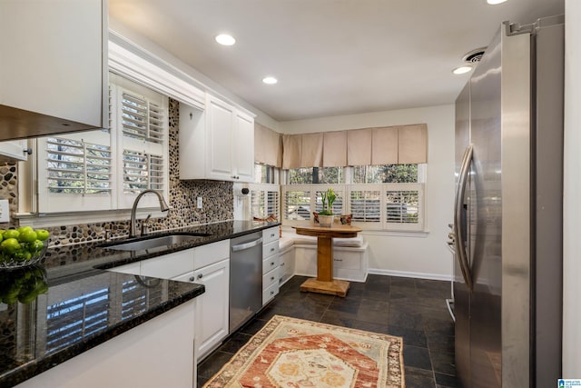 kitchen with a sink, tasteful backsplash, dark stone counters, appliances with stainless steel finishes, and white cabinets