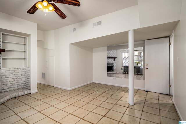 spare room featuring visible vents, built in shelves, a brick fireplace, ceiling fan, and light tile patterned floors