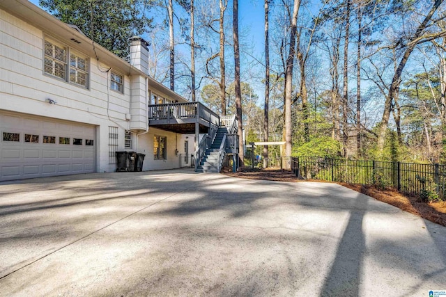 view of side of property featuring fence, a wooden deck, a chimney, stairs, and concrete driveway