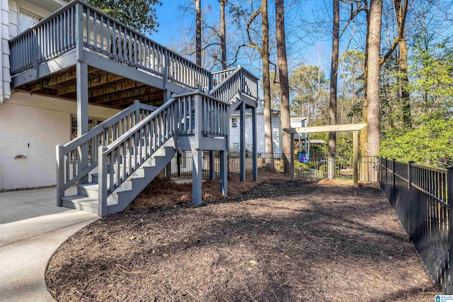 view of property exterior with a wooden deck, concrete block siding, stairs, and fence