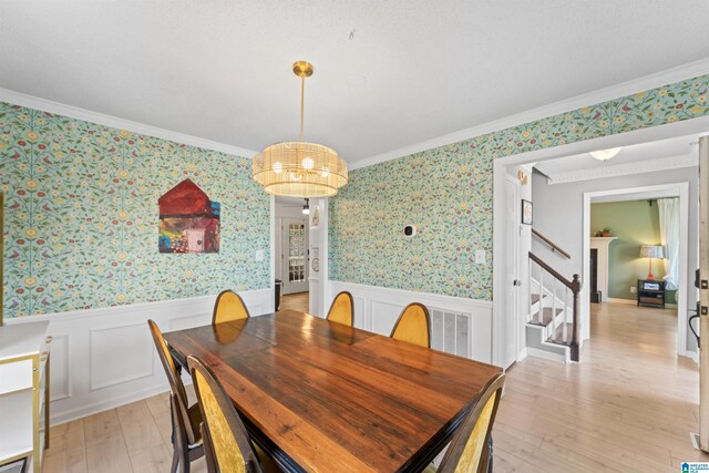 dining space with wallpapered walls, crown molding, light wood finished floors, and wainscoting