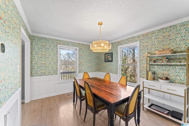 dining space featuring a wainscoted wall, a textured ceiling, light wood-style flooring, and wallpapered walls