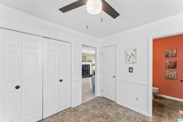 bedroom featuring a fireplace with raised hearth, a ceiling fan, ensuite bathroom, a closet, and baseboards