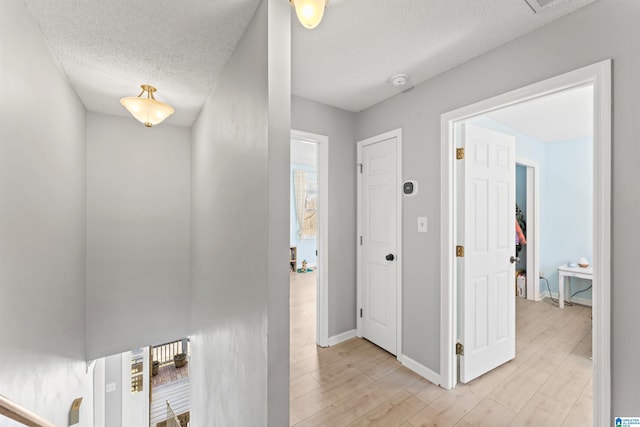 corridor featuring baseboards, light wood-style floors, and a textured ceiling