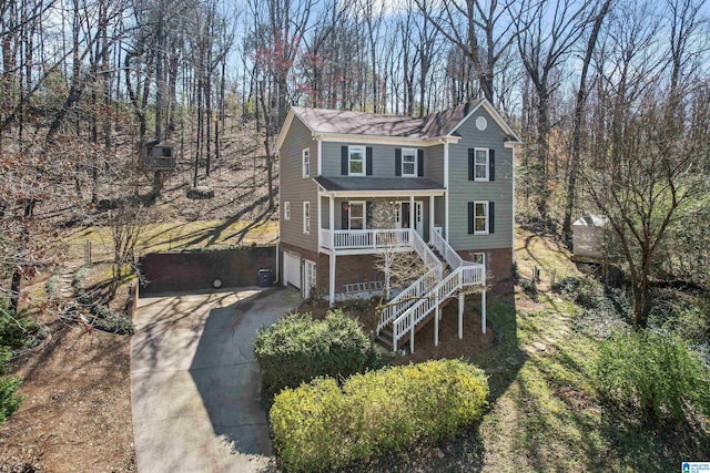 view of front of home featuring covered porch, driveway, an attached garage, and stairs