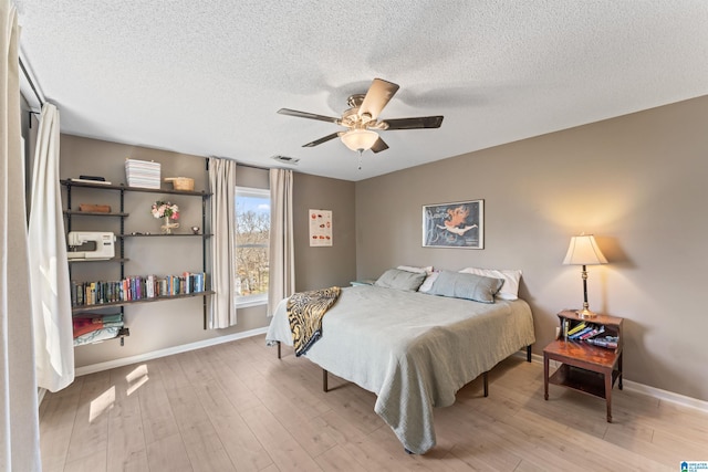 bedroom featuring visible vents, a textured ceiling, baseboards, and wood finished floors