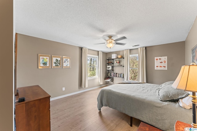 bedroom featuring visible vents, ceiling fan, baseboards, wood finished floors, and a textured ceiling