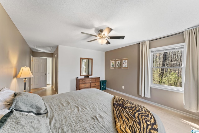 bedroom with a ceiling fan, baseboards, attic access, a textured ceiling, and light wood-type flooring