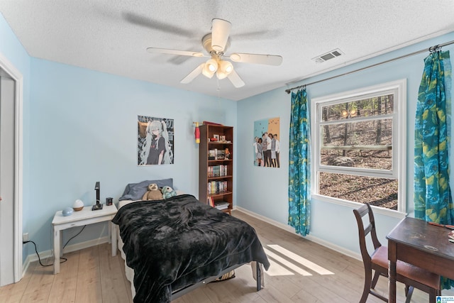 bedroom featuring visible vents, baseboards, light wood-style floors, and a textured ceiling