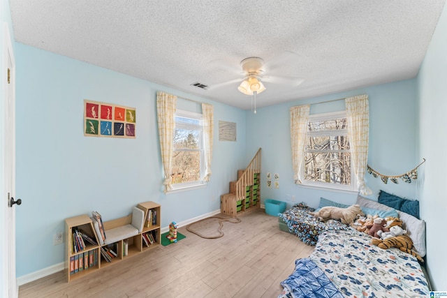 bedroom featuring a ceiling fan, visible vents, wood finished floors, baseboards, and a textured ceiling