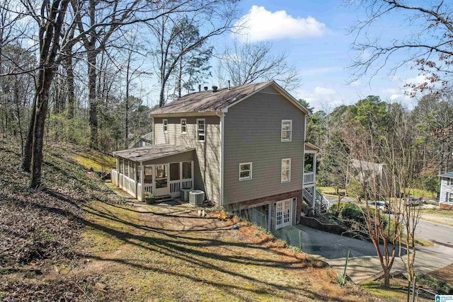 view of property exterior with an attached garage, central air condition unit, stairs, a sunroom, and driveway