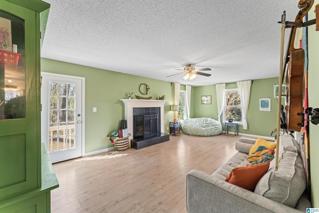 living room with light wood-style flooring, a textured ceiling, a fireplace, baseboards, and ceiling fan