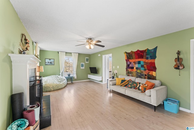 living area with baseboards, a textured ceiling, light wood-style flooring, and a ceiling fan