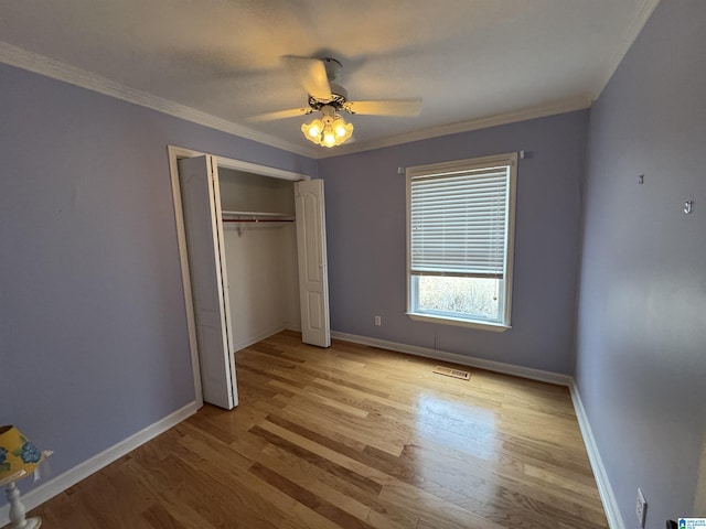 unfurnished bedroom with baseboards, visible vents, light wood-style flooring, ornamental molding, and a closet