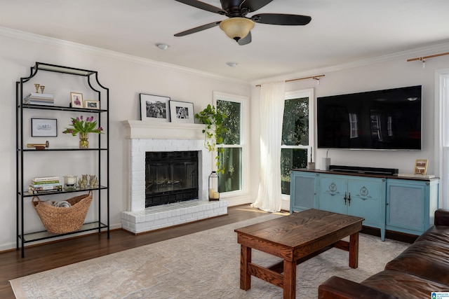 living area featuring a brick fireplace, crown molding, a ceiling fan, and wood finished floors