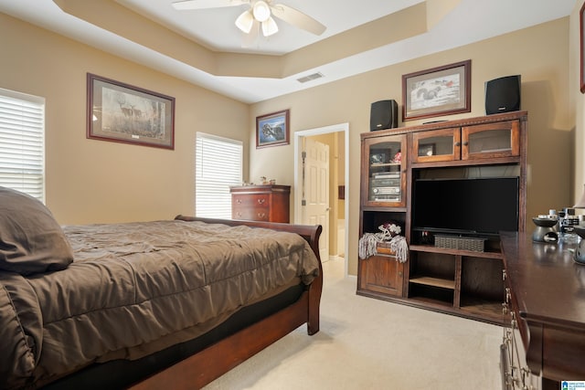 bedroom with light carpet, visible vents, ceiling fan, and a tray ceiling