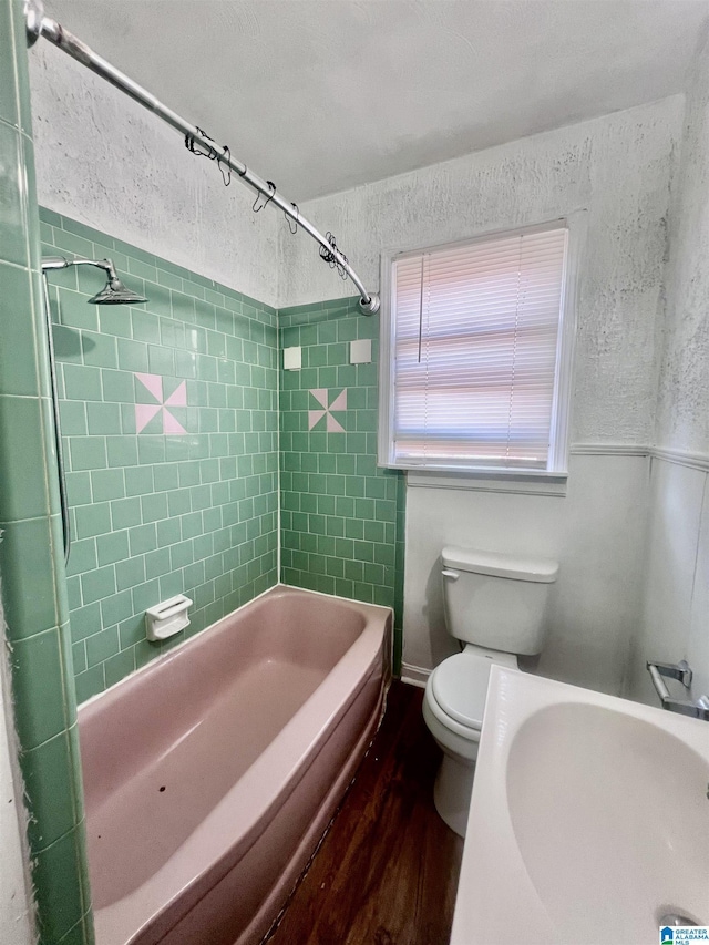 bathroom with tub / shower combination, toilet, a textured wall, and wood finished floors