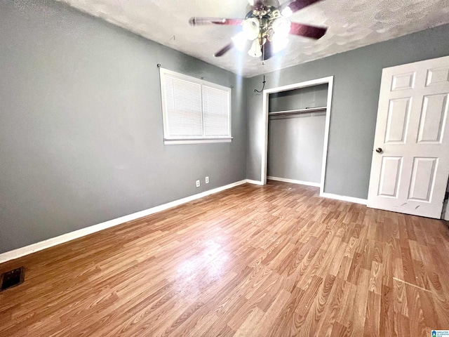 unfurnished bedroom with wood finished floors, visible vents, baseboards, ceiling fan, and a closet