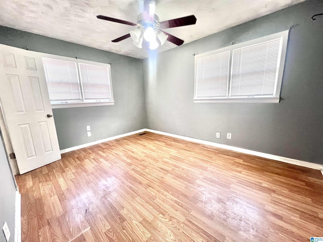 unfurnished room with ceiling fan, a textured ceiling, baseboards, and wood finished floors