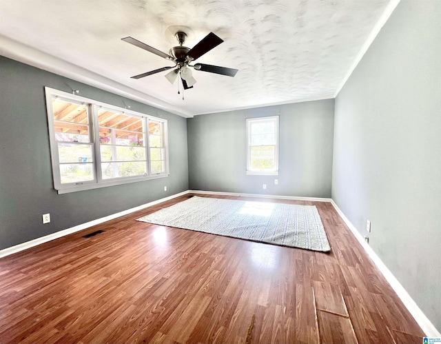 spare room featuring a ceiling fan, visible vents, wood finished floors, baseboards, and crown molding