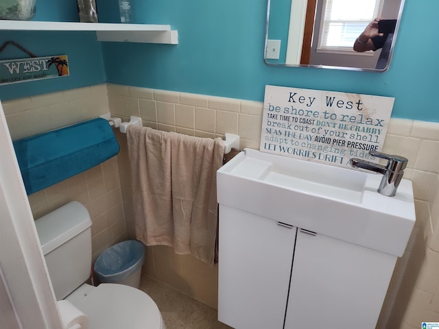 bathroom featuring a wainscoted wall, toilet, tile walls, and vanity