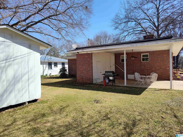 back of property with a yard, a patio, brick siding, and a chimney