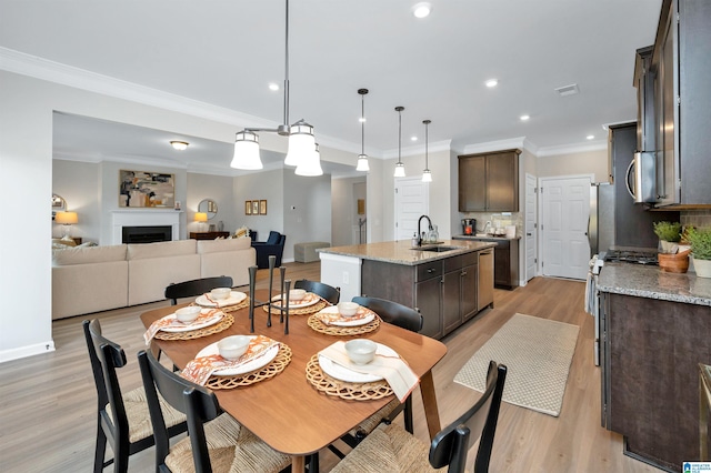 dining space featuring light wood-style flooring, ornamental molding, recessed lighting, a fireplace, and baseboards