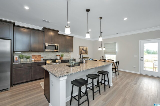 kitchen featuring backsplash, crown molding, light stone countertops, a kitchen bar, and stainless steel appliances