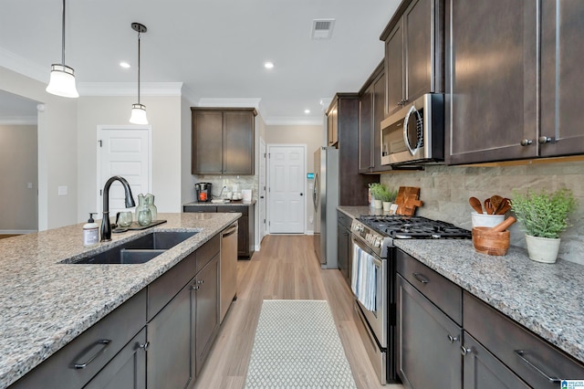 kitchen with a sink, light stone counters, dark brown cabinetry, and appliances with stainless steel finishes