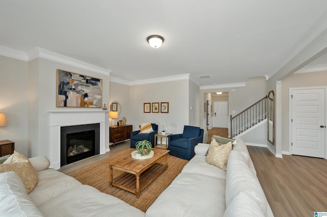 living area with stairway, wood finished floors, baseboards, ornamental molding, and a glass covered fireplace