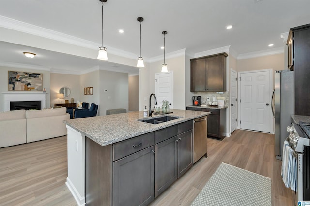 kitchen featuring a sink, light stone counters, appliances with stainless steel finishes, a fireplace, and dark brown cabinets