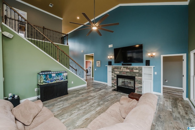 living area featuring stairway, a stone fireplace, a towering ceiling, wood finished floors, and a ceiling fan